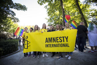 Ungdommer på Pride står bak et Amnesty-banner og smiler til kamera. 